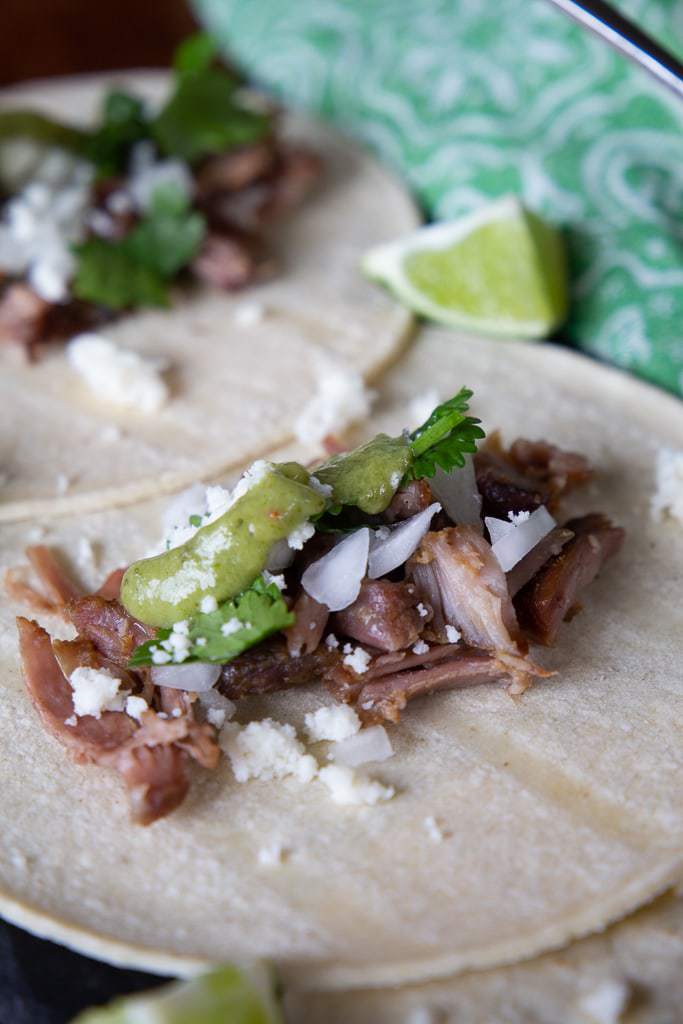 carnitas tacos garnished with salsa verde and queso fresco