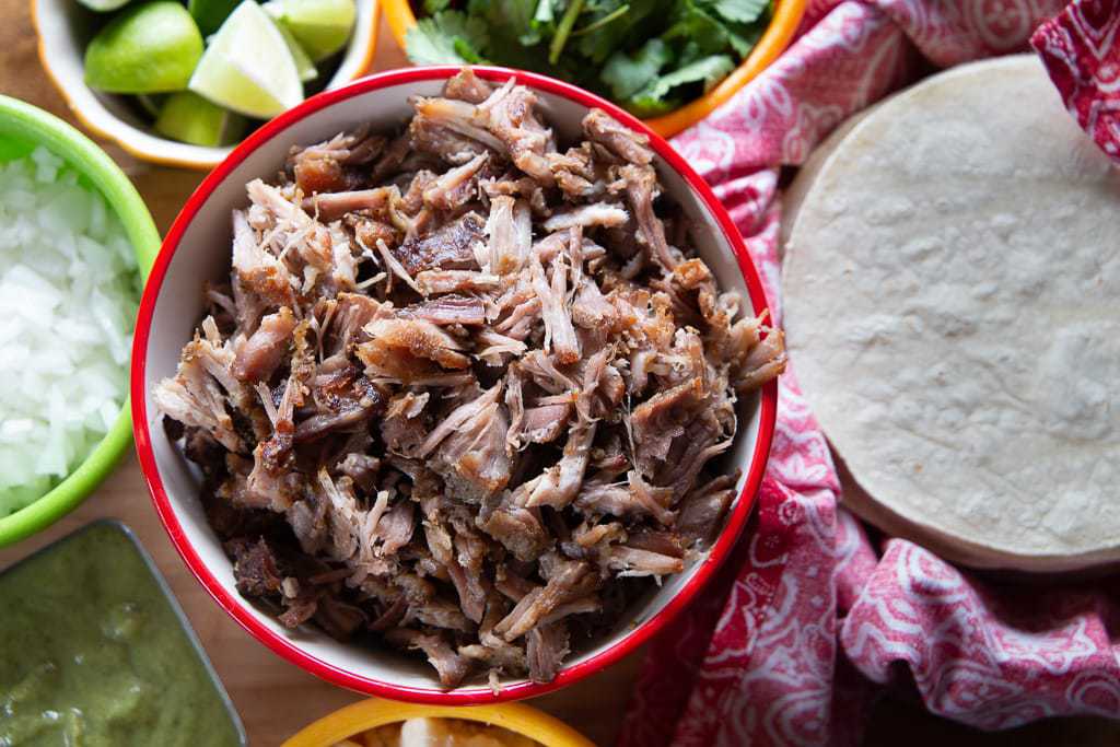 mexican shredded pork with tortillas, lime, onion and cilantro garnish