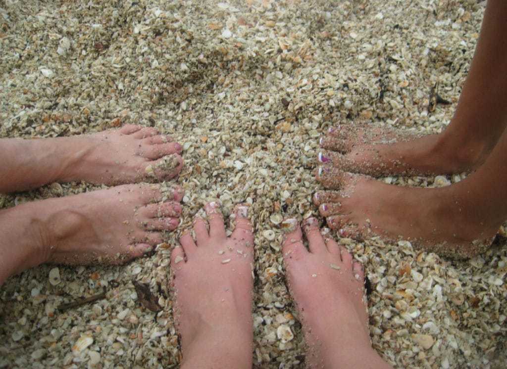 Three pairs of feet buried in the shell filled sand at playa conchal.