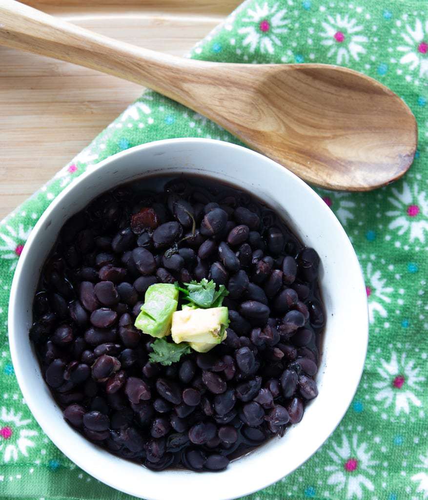 White ceramic bowl of Costa-Rican style slow cooked black beans topped with diced avocado and cilantro leaves.