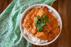 White bowl of chicken tikka masala on a pale green cloth.