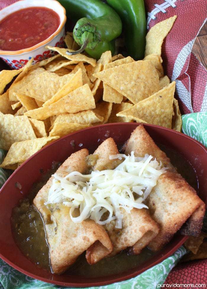 Series of chile rellenos topped with shredded cheese in a red bowl surrounded by fresh tortilla chips.