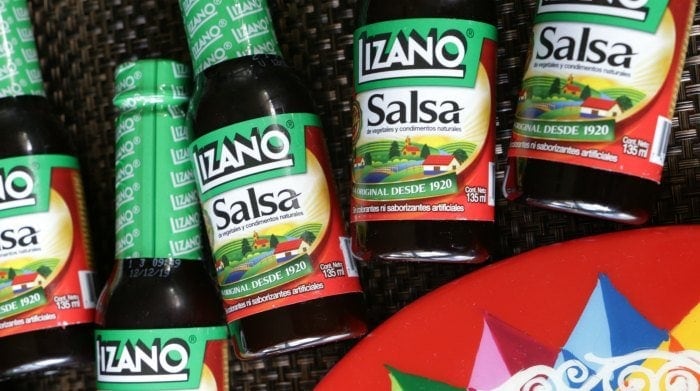 Bottles of Salsa Lizano lined up on a woven black mat.