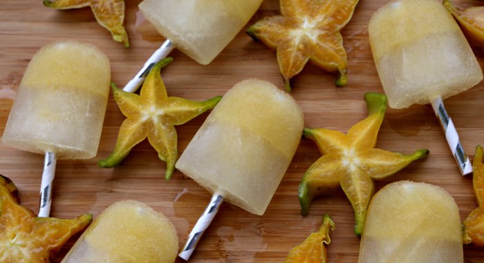Starfruit popsicles on wooden cutting board with yellow 5 pointed carambola fruit.