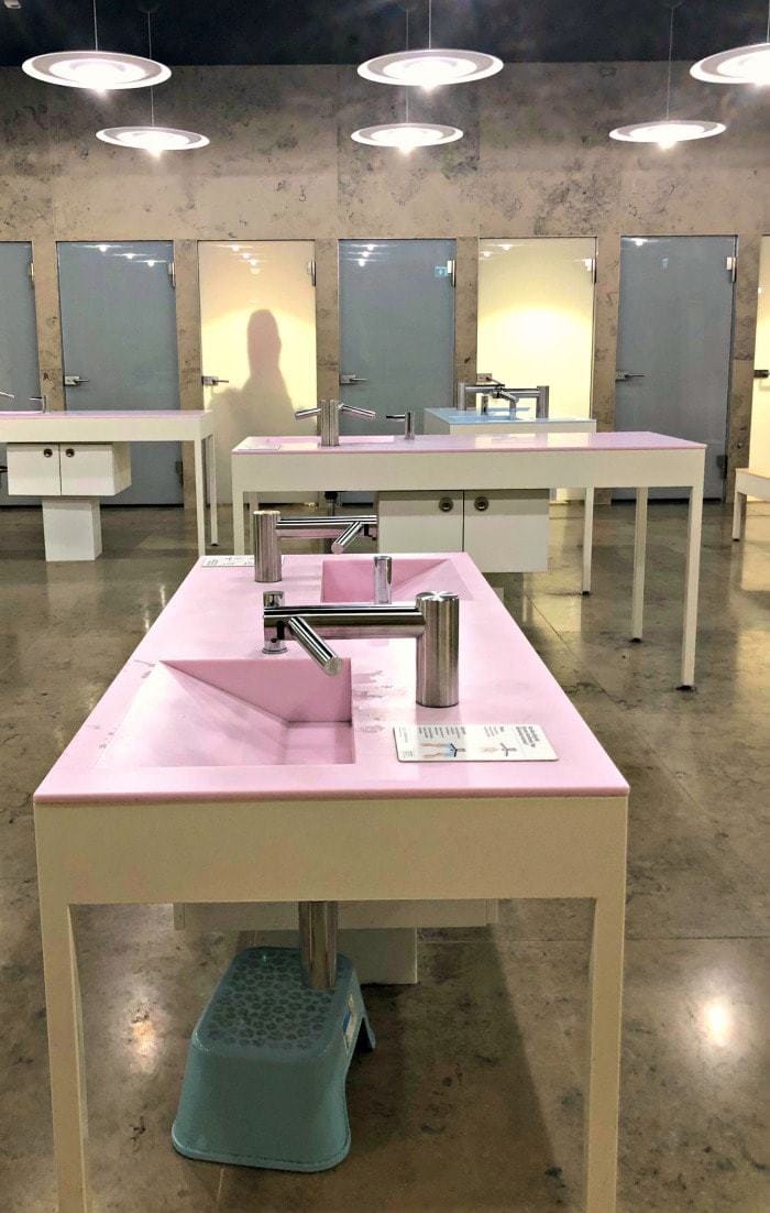pink bathroom sink with stalls in background