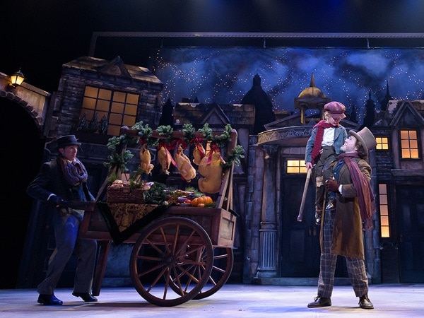 Actors in front of a Victorian-style set perform a scene in a Christmas Carol.