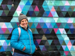 Woman wearing a winter outfit posing in front of a wall patterned with painted triangles.