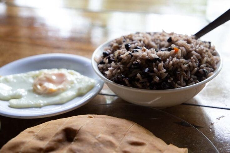 Beans and rice, fried egg, and pan casero together on a wooden tabletop.