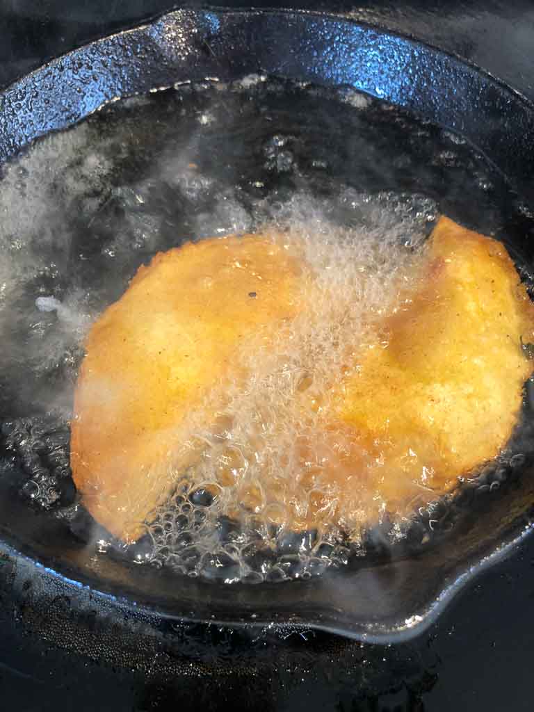 Two empanadas frying in a cast-iron skillet.