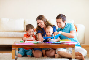 Young and smiling family with two children reading and drawing at their coffee table.