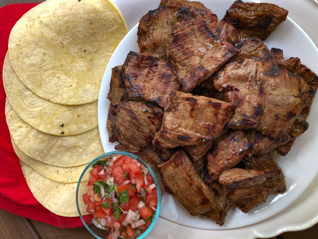 White plate of carne asada with salsa and tortillas.