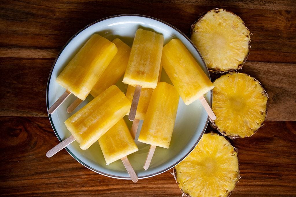 Aerial photo of pineapple popsicles on a plate ringed by whole slices of pineapple fruit.