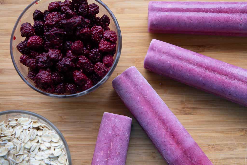 Blackberry oatmeal ice pops ringed around a bowl of blackberries.