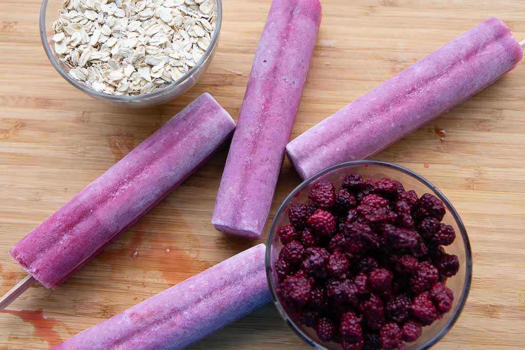 Blackberry oatmeal ice pops and bowls of berries and oats arranged on a wooden board.