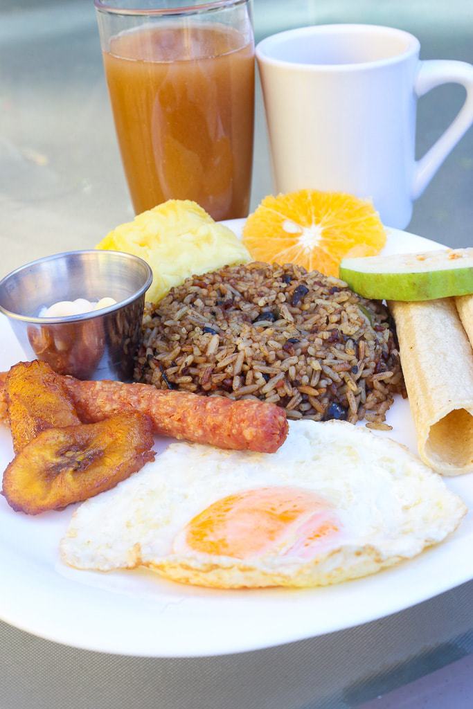 Traditional Costa Rican breakfast featuring gallo pinto, fruit, fried egg, plantains, fresh fruit, and a juice drink.