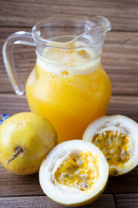 Pitcher of passion fruit juice beside halved yellow passion fruits.