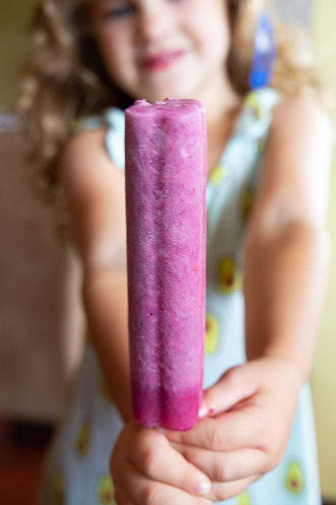 Smiling girl holding a creamy blackberry popsicle.