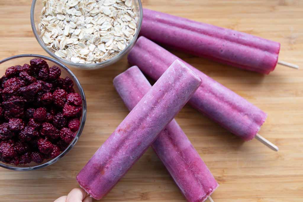 Series of blackberry oatmeal popsicles with two bowls of berries and oats.