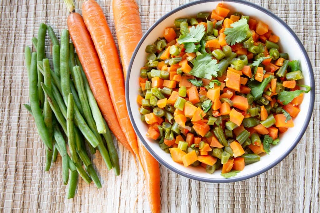 Bundles of carrots and green beans alongside a bowl of finely chopped carrots and beans.