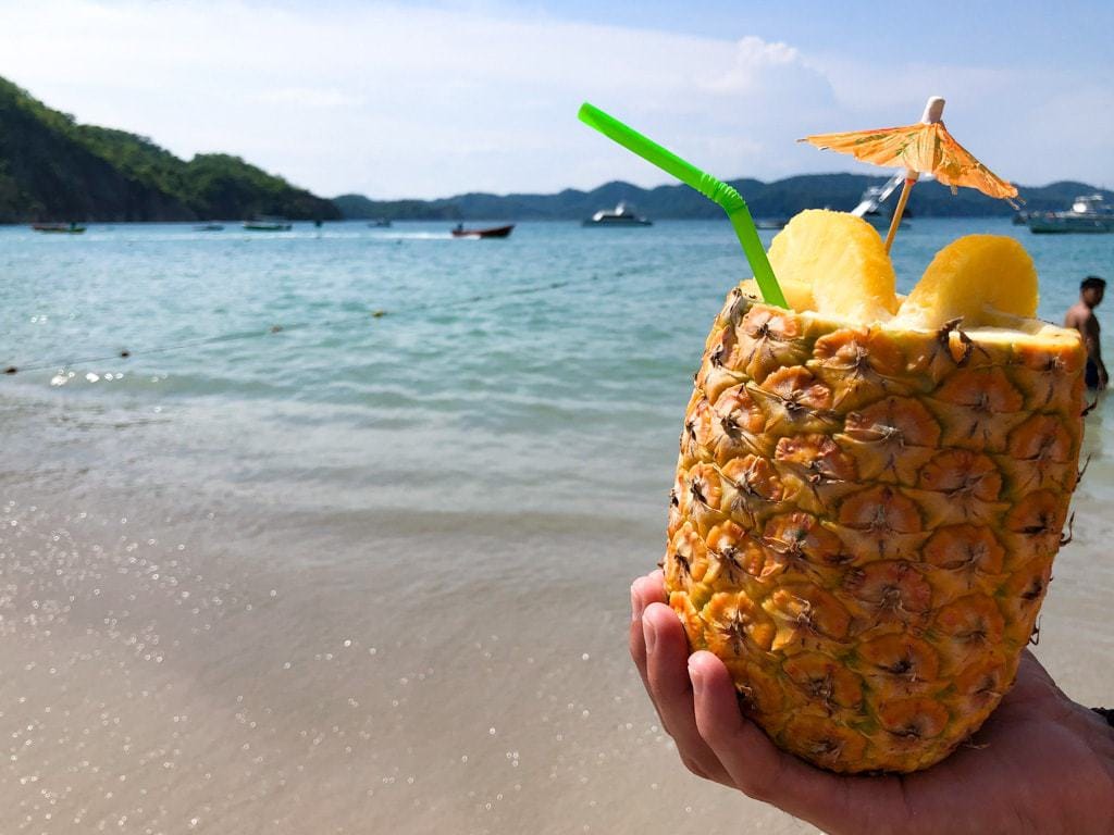 Pina colada in a hollowed out pineapple with the beach in the background.