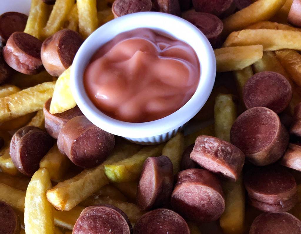 Close up of hot dog and french fry medley surrounding a bowl of pink sauce.