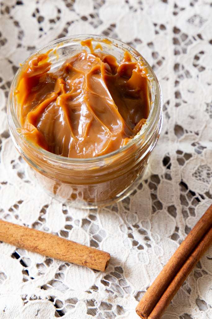 Jar of dulce de leche with two cinnamon sticks in front of it.