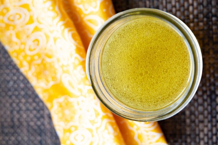 Close up of a jar of chicken broth on a grey mat with a yellow patterned napkin.
