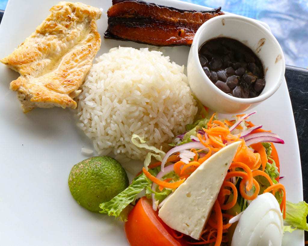 costa rican casado on square white plate with side of black beans and salad.