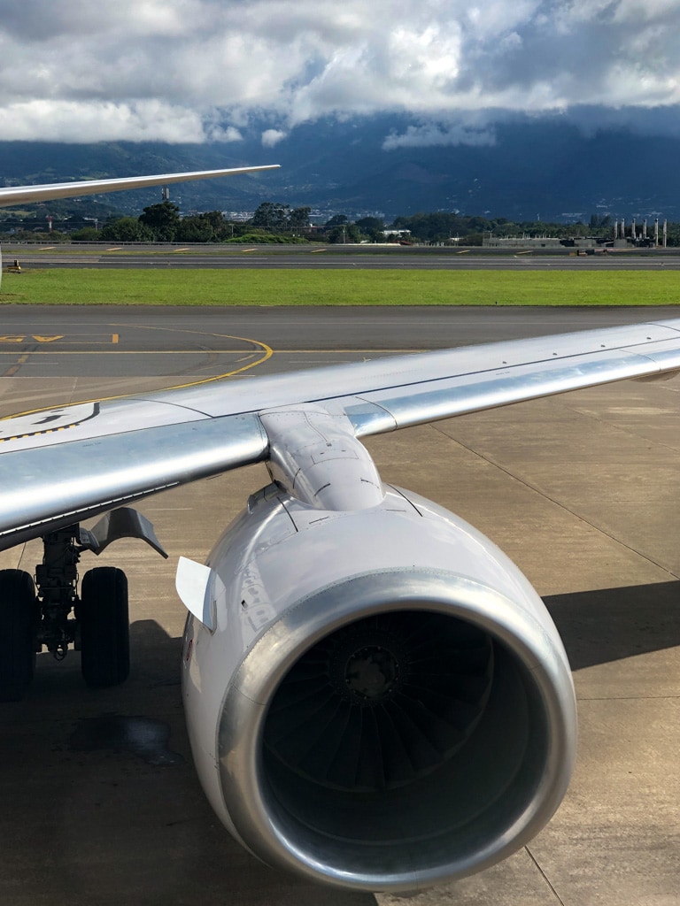 airplane wing on costa rican tarmac with mountains in distance.