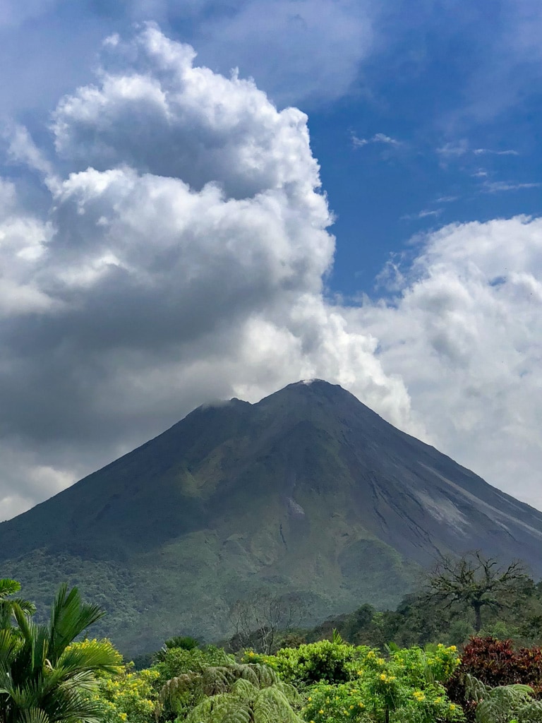 Costa rican volcano with tropical forest and puffy white clouds.